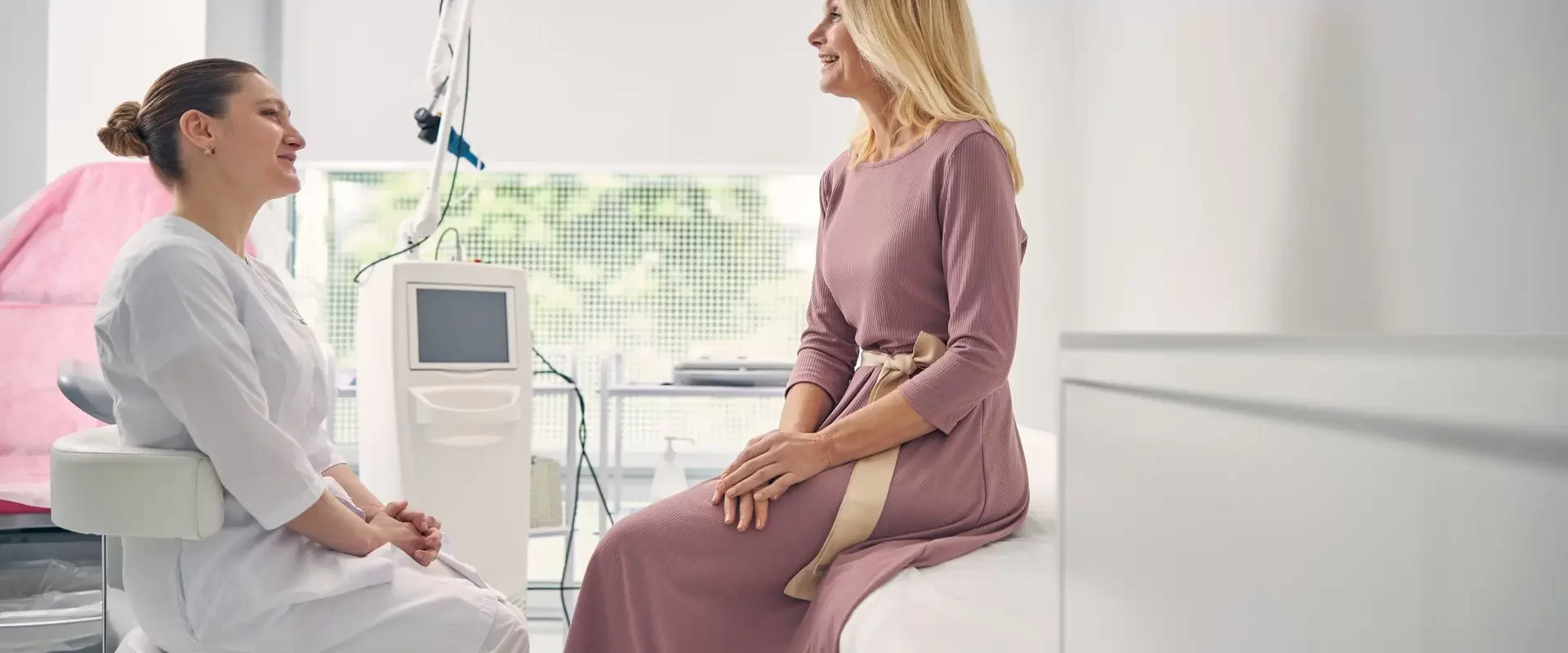 Pleased smiling female medical worker sitting while listening to her patient in beauty clinic
