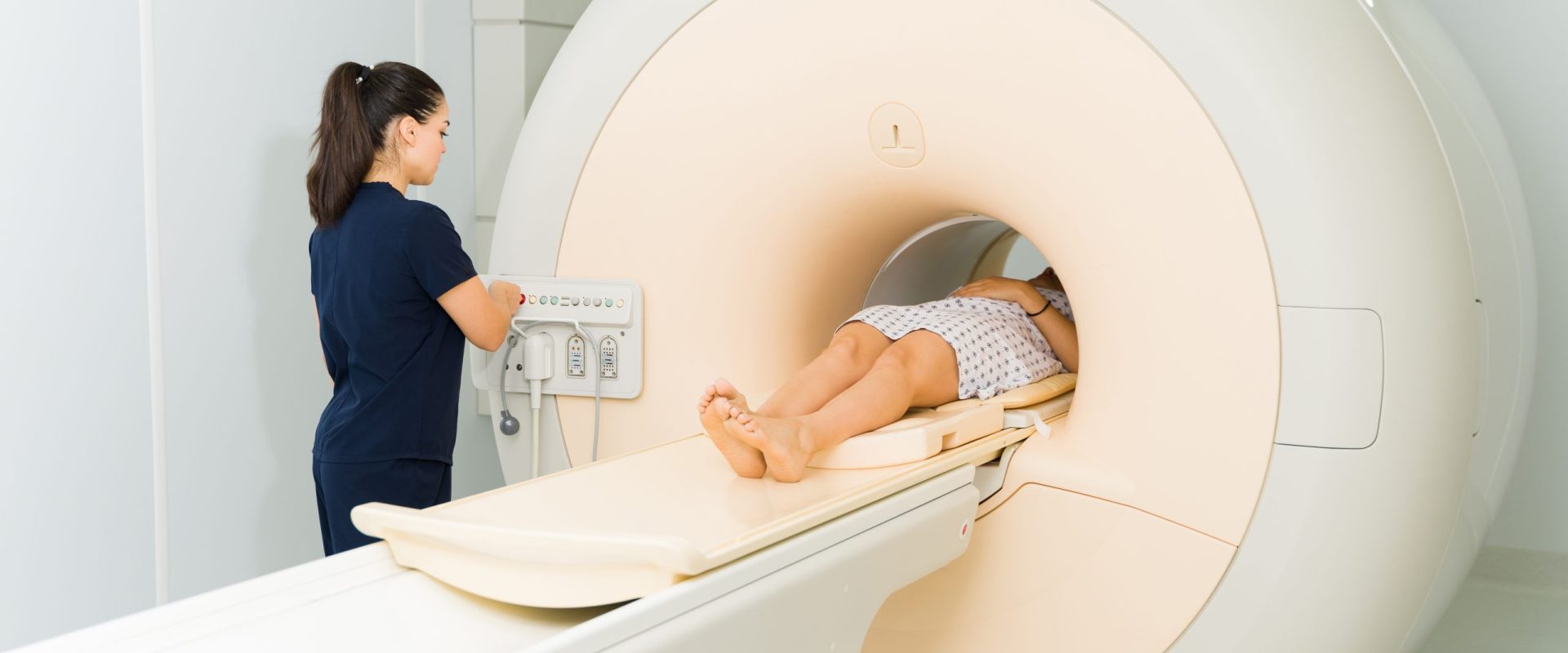 Female radiologist technician starting the button on MRI machine while doing a brain magnetic resonance exam on a young woman at the hospital